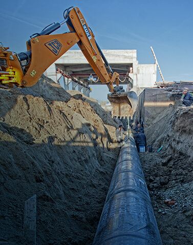 Excavator laying pipe in a trench